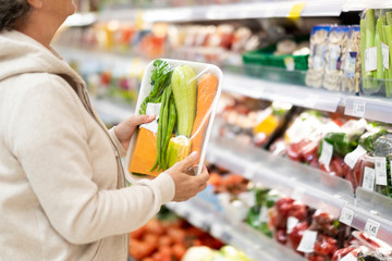 Side view of a senior woman at the supermarket checking the product before to buy. Many products on offer in the refrigerated counter