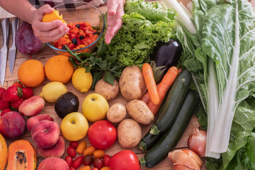 A wooden cutboard  full of fruits and vegetables. One  woman only prepare a vegetarian fruit salad - bright light from the window