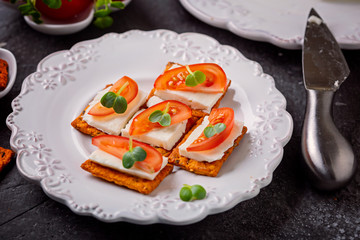Fototapeta na wymiar Canape from crackers with soft cheese stracchino , tomato slice and green leaf. 