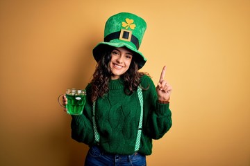Beautiful curly hair woman wearing hat drinking jar of green beverage on saint patricks day surprised with an idea or question pointing finger with happy face, number one