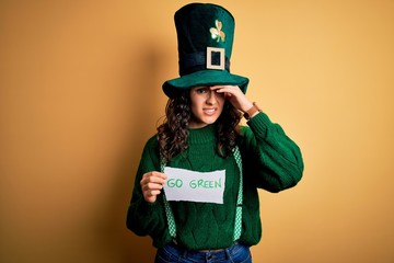 Beautiful curly hair woman wearing hat with clover holding banner with go green message stressed with hand on head, shocked with shame and surprise face, angry and frustrated. Fear and upset 