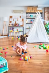Young beautiful toddler sitting on the floor playing with wooden train toy at kindergaten