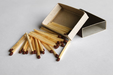 Wooden protective matches are scattered around a cardboard matchbox.