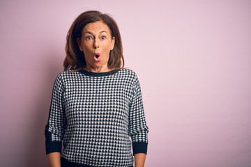 Middle age beautiful woman wearing casual sweater standing over isolated pink background afraid and shocked with surprise expression, fear and excited face.