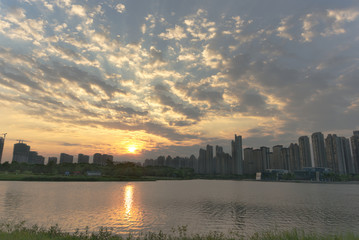 Fototapeta na wymiar Sunset scenery of a city park; sunset reflects on a lake surface in cloudy weather