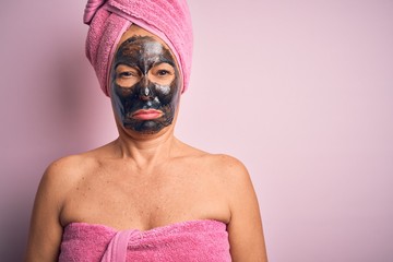 Middle age brunette woman wearing beauty black face mask over isolated pink background depressed and worry for distress, crying angry and afraid. Sad expression.