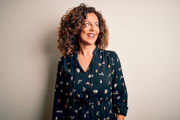 Middle age beautiful woman wearing casual dress standing over isolated white background looking away to side with smile on face, natural expression. Laughing confident.