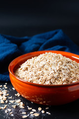 Healthy food concept organic whole-grain Rolled oats in orange bowl with blue napkins on black slate stone background