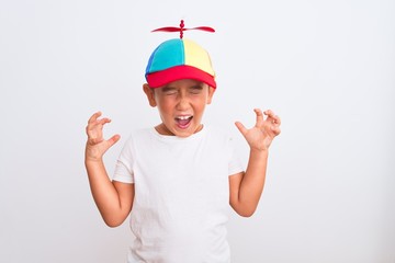 Beautiful kid boy wearing fanny colorful cap with propeller over isolated white background celebrating mad and crazy for success with arms raised and closed eyes screaming excited. Winner concept