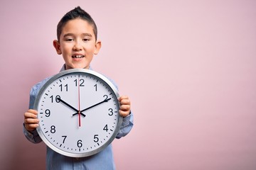 Young little boy kid holding big minute clock over isolated pink background with a happy face...