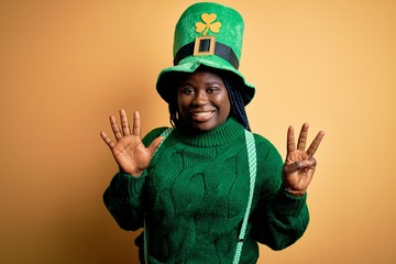 Plus size african american woman with braids wearing green hat with clover on st patricks day showing and pointing up with fingers number eight while smiling confident and happy.