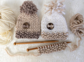 Fototapeta na wymiar knitted natural colours baby hats with wool and knitting needles 