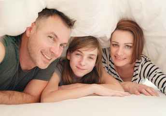 Happy family in bedroom: mother ,father and daughter under the blanket in bed at home