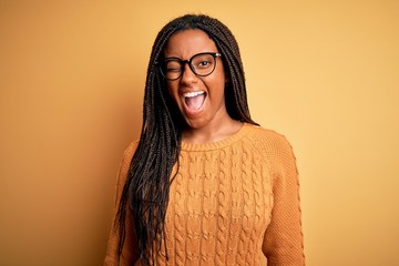Young african american smart woman wearing glasses and casual sweater over yellow background...