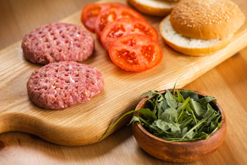Buns, raw beef cutlets, tomatoes and herbs for burgers cooking