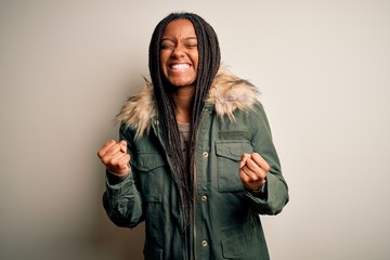 Young african american woman wearing winter parka coat over isolated background very happy and excited doing winner gesture with arms raised, smiling and screaming for success. Celebration concept.