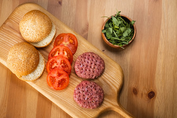 Buns, raw beef cutlets, tomatoes and herbs for burgers cooking