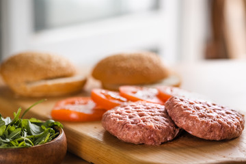 Buns, raw beef cutlets, tomatoes and herbs for burgers cooking