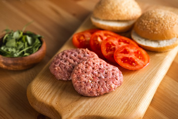 Buns, raw beef cutlets, tomatoes and herbs for burgers cooking