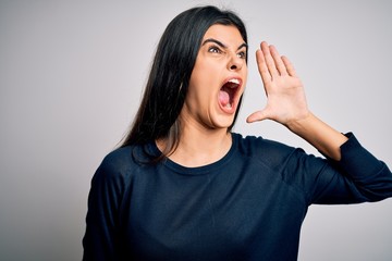 Young beautiful brunette woman wearing casual sweater standing over white background shouting and screaming loud to side with hand on mouth. Communication concept.