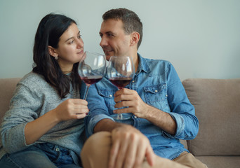 Young romantic couple sitting on sofa at home drinking red wine.