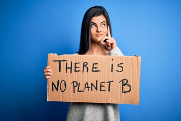 Young beautiful brunette activist woman holding banner protesting to care the planet serious face...