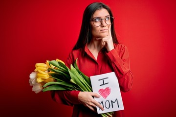 Young beautiful woman with blue eyes holding love mom message and tulips on mothers day serious...