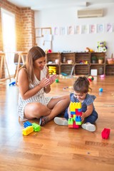 Fototapeta premium Young beautiful teacher and toddler playing with building blocks toy at kindergarten