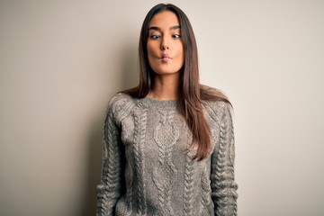 Young beautiful brunette woman wearing casual sweater over isolated white background making fish face with lips, crazy and comical gesture. Funny expression.