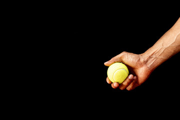 A man's hand holding a tennis ball on a black background.