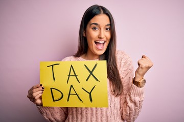 Young beautiful brunette woman holding paper with tax day message over pink background screaming...
