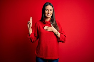 Young beautiful brunette woman wearing casual sweater over isolated red background smiling swearing...