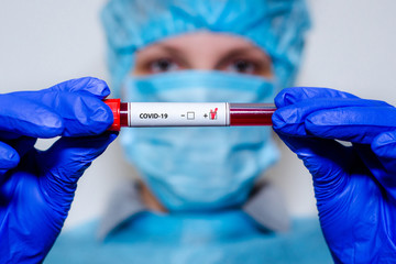 Medical laboratory assistant holding test tube with positive Coronavirus test blood sample.