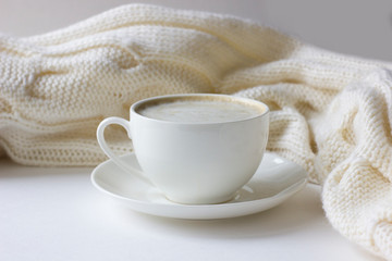 White coffee cup with plate on knitted scarf background.