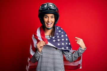 Young beautiful patriotic motorcyclist woman wearing moto helmet and united states flag very happy pointing with hand and finger