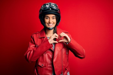 Young beautiful brunette motorcyclist woman wearing motorcycle helmet and red jacket smiling in...