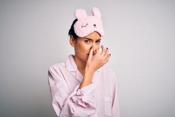 Young beautiful brunette woman wearing pajama and sleep mask over white background smelling...