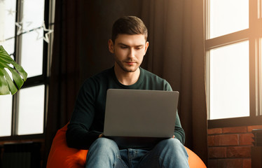 Busy Freelancer Working On Laptop In Beanbag Chair At Home