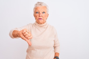 Senior grey-haired woman wearing turtleneck sweater standing over isolated white background looking unhappy and angry showing rejection and negative with thumbs down gesture. Bad expression.
