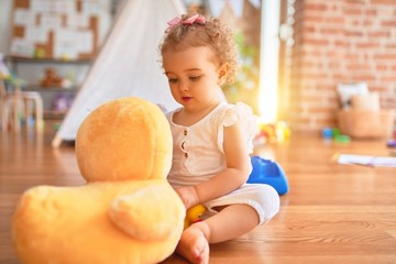 Beautiful caucasian infant playing with toys at colorful playroom. Happy and playful cuddling stuffed animal at kindergarten.