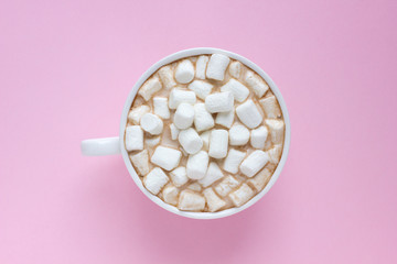 Top view of white cup with hot cocoa with marshmallows on pink background.