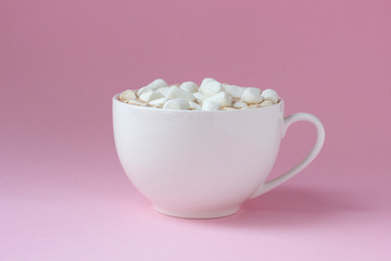 White cup with hot cocoa with marshmallows on pink background.