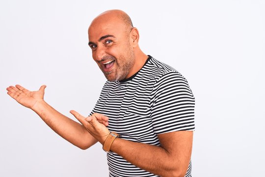 Middle age handsome man wearing striped navy t-shirt over isolated white background amazed and smiling to the camera while presenting with hand and pointing with finger.
