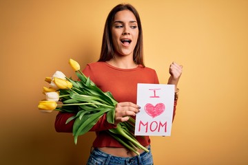 Beautiful woman celebrating mothers day holding love mom message and bouquet of tulips pointing and showing with thumb up to the side with happy face smiling