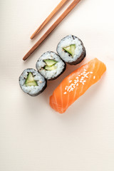 Sushi with salmon and cucumber roll with chopsticks on a light beige background, nigiri sake and futomaki