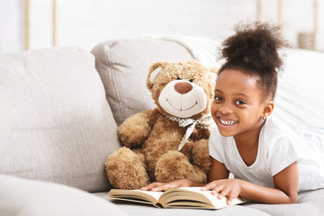 Cute afro baby girl playing with teddy bear, reading book