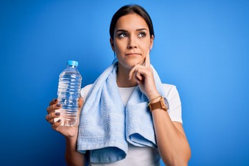 Young beautiful brunette sportswoman wearing towel drinking bottle of water to refreshment serious face thinking about question, very confused idea