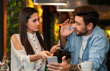 Jealous Girlfriend Showing Boyfriend Message On Phone Sitting In Cafe