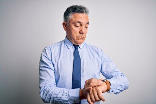 Middle age handsome grey-haired business man wearing elegant shirt and tie Checking the time on wrist watch, relaxed and confident