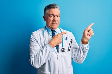 Middle age handsome grey-haired doctor man wearing coat and blue stethoscope Pointing aside worried...